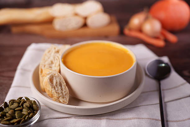 cozy autumn table setting with creamy pumpkin soup in a ceramic bowl garnished with fresh bread and pepitas, highlighting warm earthy tones and rustic kitchen ambiance, arranged, layered, hygge