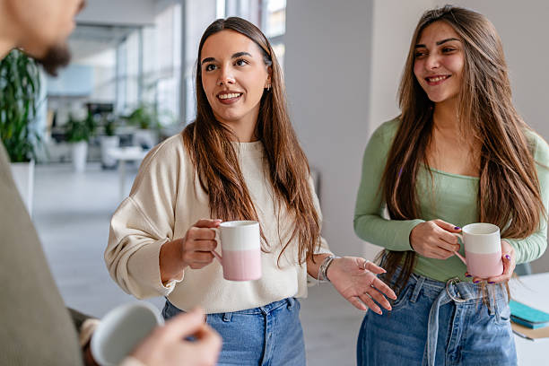istock Two adults engage in conversation while holding coffee mugs in a modern office space during working hours 2252604089