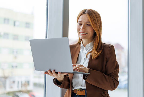 istock Businesswoman standing in office using laptop smiling 2252605259