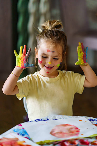 Young child creating art with messy hands covered in bright paint, smiling.