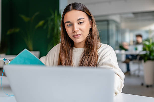 istock Young adult woman engages in work at a modern office, using technology while writing in her notebook 2252610120