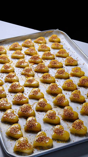 Close-up of a baker’s hand using a silicone brush to apply egg wash onto raw heart-shaped cookie dough arranged on a baking tray before baking.