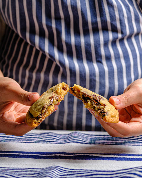 Female Hands Breaking Freshly Baked Soft Chocolate Chip Cookie in Half to Show Melted Chocolate Texture