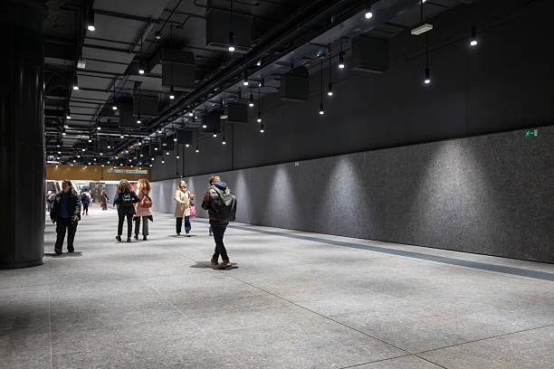 Rome, Italy - December 17, 2025: Citizens walk along a minimalist grey corridor at the Colosseo Metro Line C station, featuring specialized spotlights and a sleek industrial aesthetic.