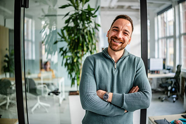 istock Professional adult stands confidently in modern office space while colleagues work in background during a busy day 2252624127