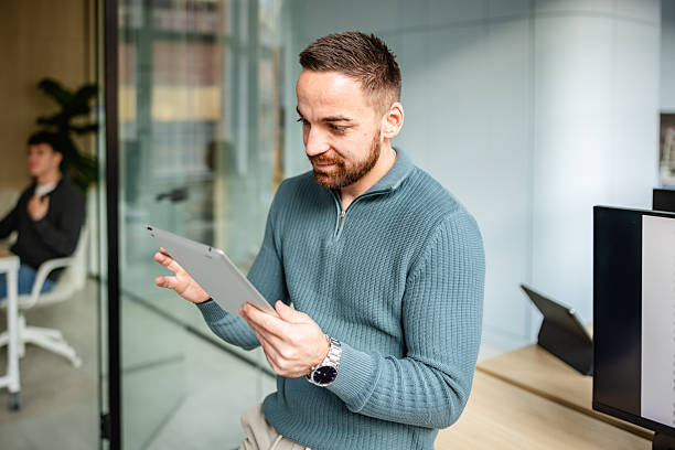 istock Professional man works with a tablet in a modern office while a colleague engages in the background during office hours 2252625648