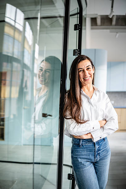 istock Professional woman stands inside modern office smiling by glass wall with reflection, engaged and ready for work 2252625893