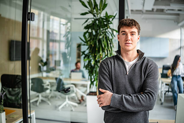istock Young professional stands in modern office space while co-workers engage in tasks focused on business activities 2252627307