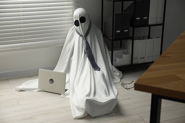 istock Overworked ghost. Man in white sheet with laptop on floor in office 2252629234