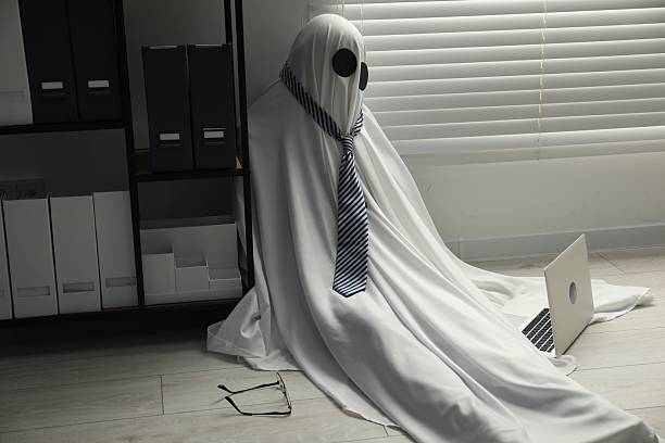 istock Overworked ghost. Man in white sheet with laptop on floor in office 2252629344