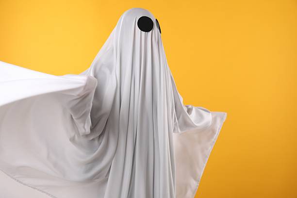 istock Creepy ghost. Person covered with white sheet on yellow background, space for text 2252629394