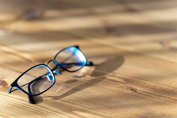 Black rimmed eyeglasses on wooden table in sunlight
