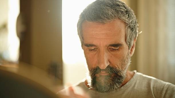 The retirement single lifestyle. Senior bachelor man doing chores at home in the early morning at sunrise, cleaning the glassware for stress management.