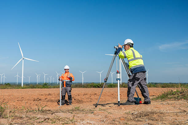 istock Engineer working at renewable energy site wind turbines examining  blueprint surveying instrument mounted tripod ensuring accurate land measurements practices in environmental industrial. 2252645339