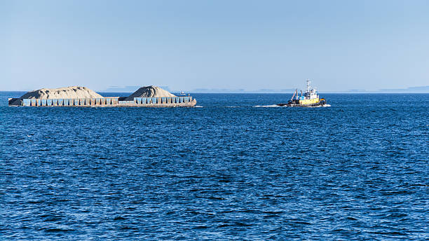 istock Tugboat  is pulling a barge of ore in open sea water 2252648363