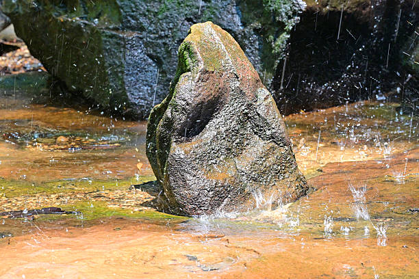 A rock at the bottom of a waterfall with drips of water