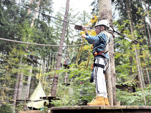 Wide shot of a boy demonstrating agility and courage while crossing a rope bridge high above the ground. Physical activity and the fight against childhood obesity.