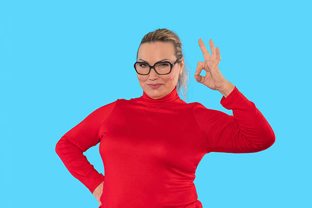 istock Woman in a red sweater makes an okay hand gesture against a bright blue background while smiling confidently in a studio setting 2252655688