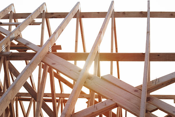 A symmetrical view of wooden roof trusses and beams in a finished attic space, showcasing precise carpentry and natural wood texture. The warm tones and clean lines emphasize structure, craftsmanship, and architectural design. The image reflects sustainable construction and interior detail.
