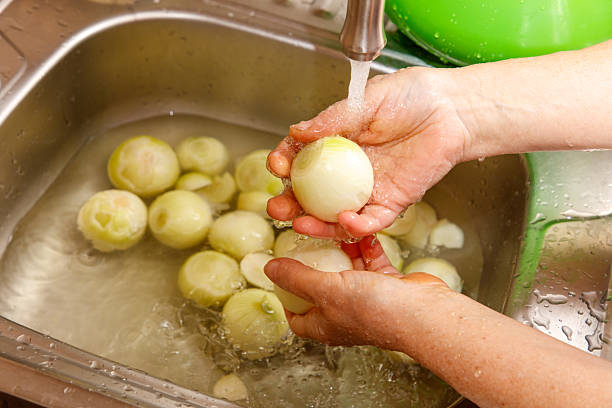 A person is washing onions in a sink. The onions are in the sink and the water is running