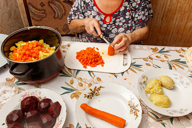 A woman is cutting carrots on a cutting board. There are several carrots on the cutting board and a bowl of carrots on the table