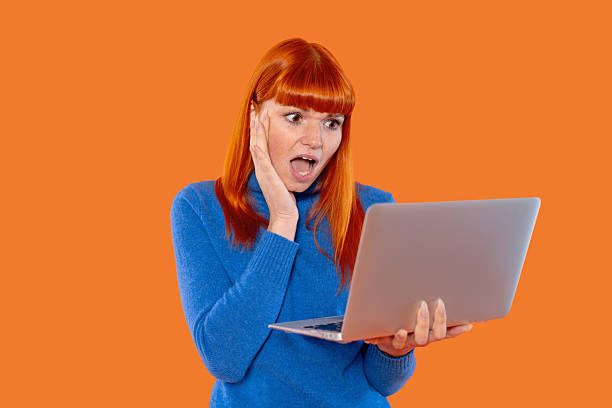 istock Surprised woman using laptop with shocked expression against a bright orange background 2252657847