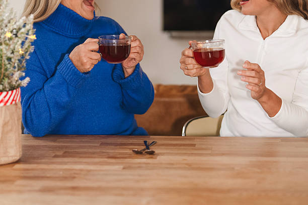 Two friends share laughter and tea at a cozy kitchen table during a relaxed afternoon gathering at home