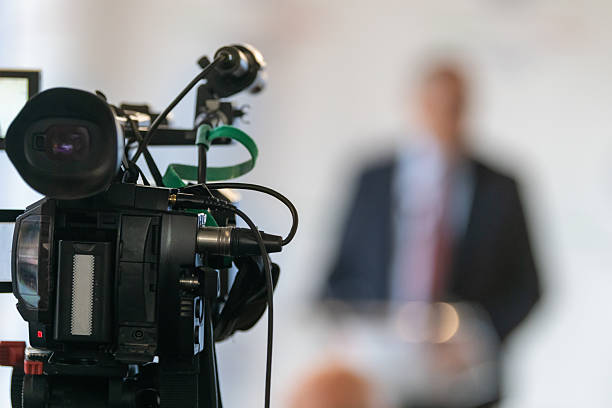 istock TV camera recording speaker at formal press conference. Highlights media coverage, professional setup, and focused communication setting. 2252669228