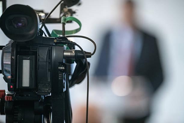 TV camera capturing live press conference with officials. Emphasizes clarity, public communication, and structured media environment.