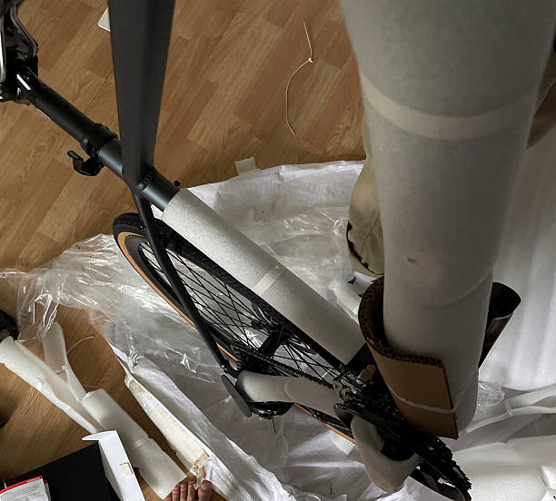 A person unwraps a bicycle surrounded by packing materials in a cluttered room