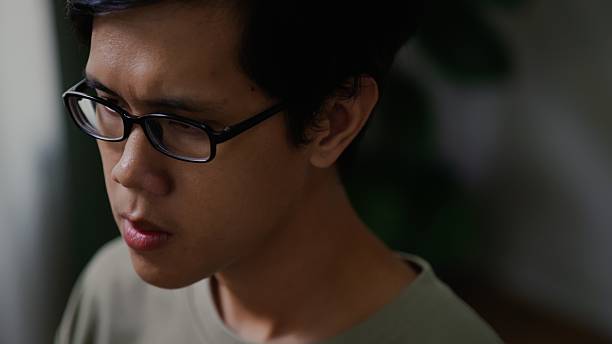 Asian man shows a serious and focused expression, reflecting deep concentration and determination. His stern facial features convey commitment, responsibility, and a thoughtful mindset. The image represents realistic human emotion, mental focus, and moments of serious decision-making.