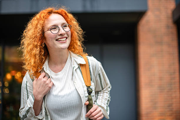 istock Young ginger woman smiles while walking outdoors with a backpack during the day in a city setting 2252679869