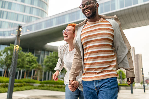 istock Young couple enjoys a fun day outdoors while holding hands and laughing together in a modern city setting 2252680038