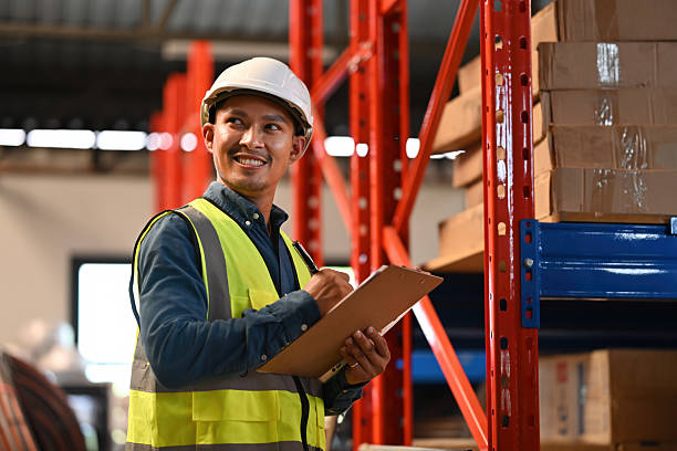 istock An Asian male warehouse worker in reflective vest and hard hat smiling while taking inventory on a clipboard 2252680504