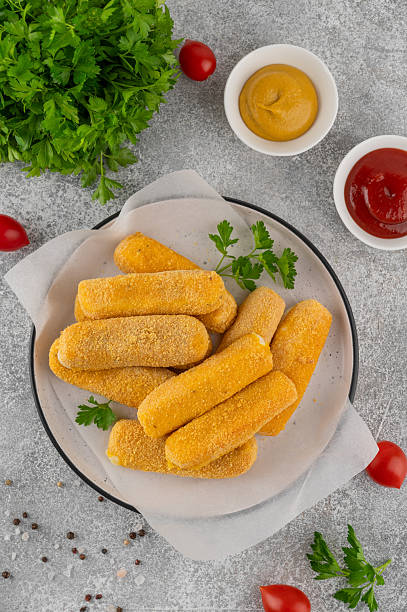 istock Crispy breaded mozzarella sticks on a plate with parsley, served with ketchup and mustard dips. Golden fried texture, appetizing snack on gray background 2252681127