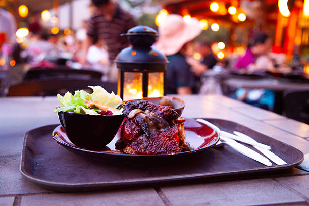 Steak and Salad Plate at Warmly Lit Outdoor Restaurant ,Dinner Meal with Bokeh Lights and Romantic Night Ambiance ,Close-Up of Barbecue Dish on Table with Blurred Background