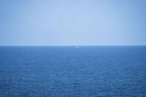 tranquil blue ocean water meeting a perfectly flat horizon, with an expansive clear sky creating a sense of calm, openness, and coastal escape