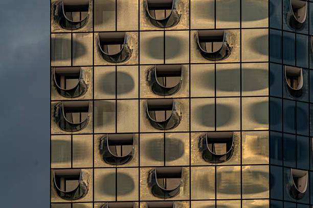 A close-up of the Elbphilharmonie’s glass facade in Hamburg, Germany, captures the golden reflections of the sunset. The iconic wave-shaped rooftop and curved window design create a dynamic, abstract interplay of light and form, highlighting the building’s innovative architecture.