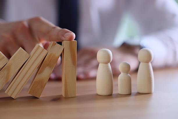 istock Risk. Man stopping domino effect to protect wooden figures at table, closeup 2252686479