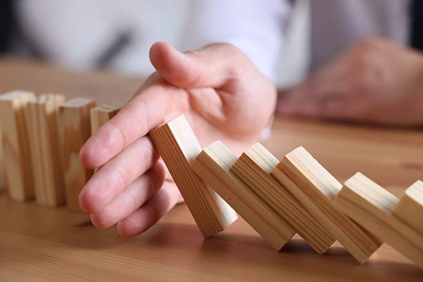 istock Risk. Man stopping domino effect at wooden table, closeup 2252686494