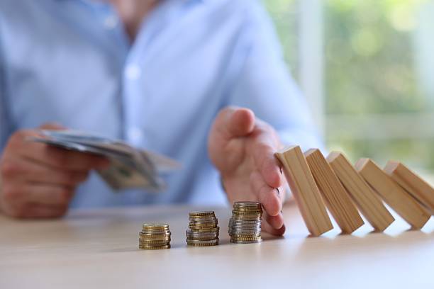 istock Risk. Man with dollars stopping domino effect to protect coins at table, closeup 2252686526