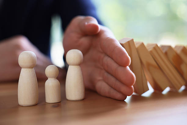 istock Risk. Man stopping domino effect to protect wooden figures at table, closeup 2252686529