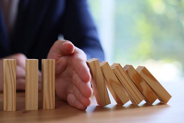 istock Risk. Man stopping domino effect at wooden table, closeup 2252686537