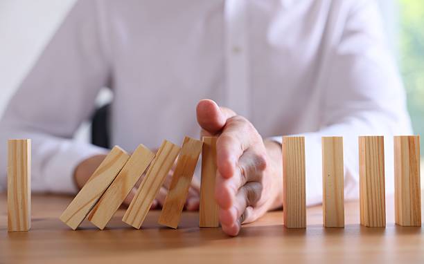istock Risk. Man stopping domino effect at wooden table, closeup 2252686542