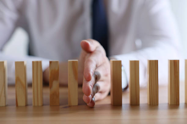 Risk. Man stopping domino effect at wooden table, closeup