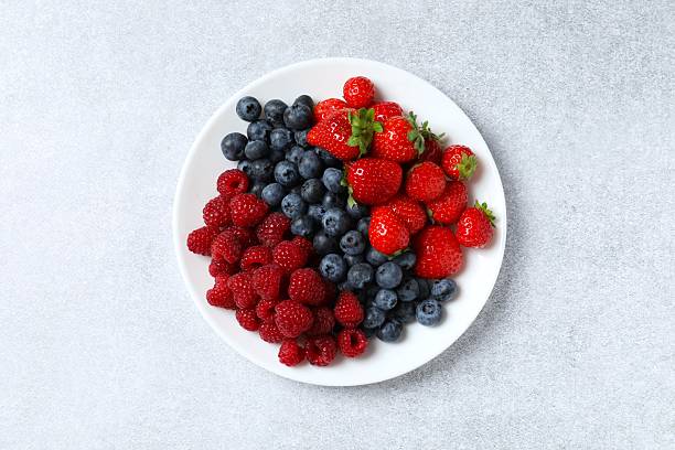 istock Different fresh ripe berries in bowl on light table, top view 2252689412