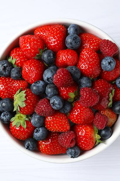 istock Different fresh ripe berries in bowl on wooden table, top view 2252689466