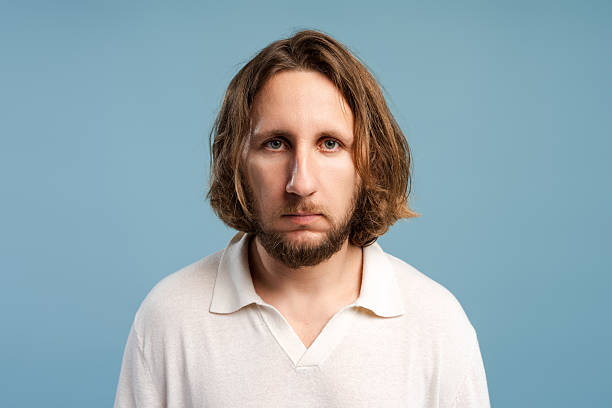 istock Man with long hair and beard standing against blue background looking at camera 2252691002
