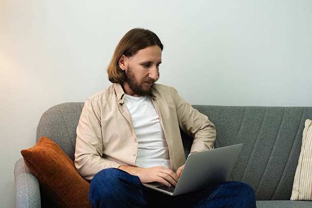 istock Man typing on laptop remotely from home sofa, focusing on work 2252692091
