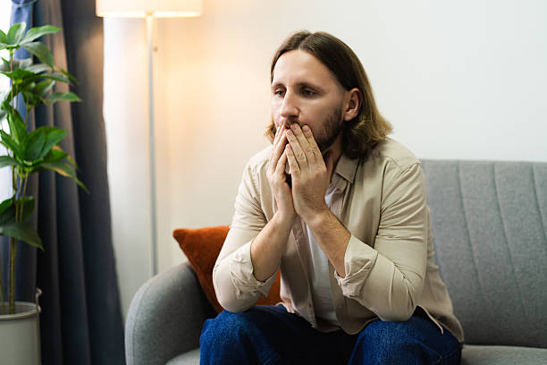 istock Young adult man feeling sad, anxious, and worried while sitting on sofa 2252692098